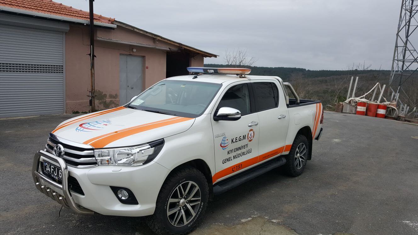 Profesyonelce giydirilmiş beyaz pick-up, açık havada park halinde, şirket bilgileri net bir şekilde sergileniyor.