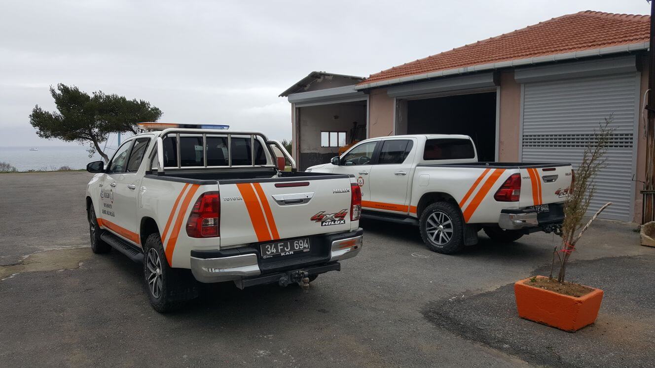 Profesyonelce giydirilmiş beyaz pick-up, açık havada park halinde, şirket bilgileri net bir şekilde sergileniyor.